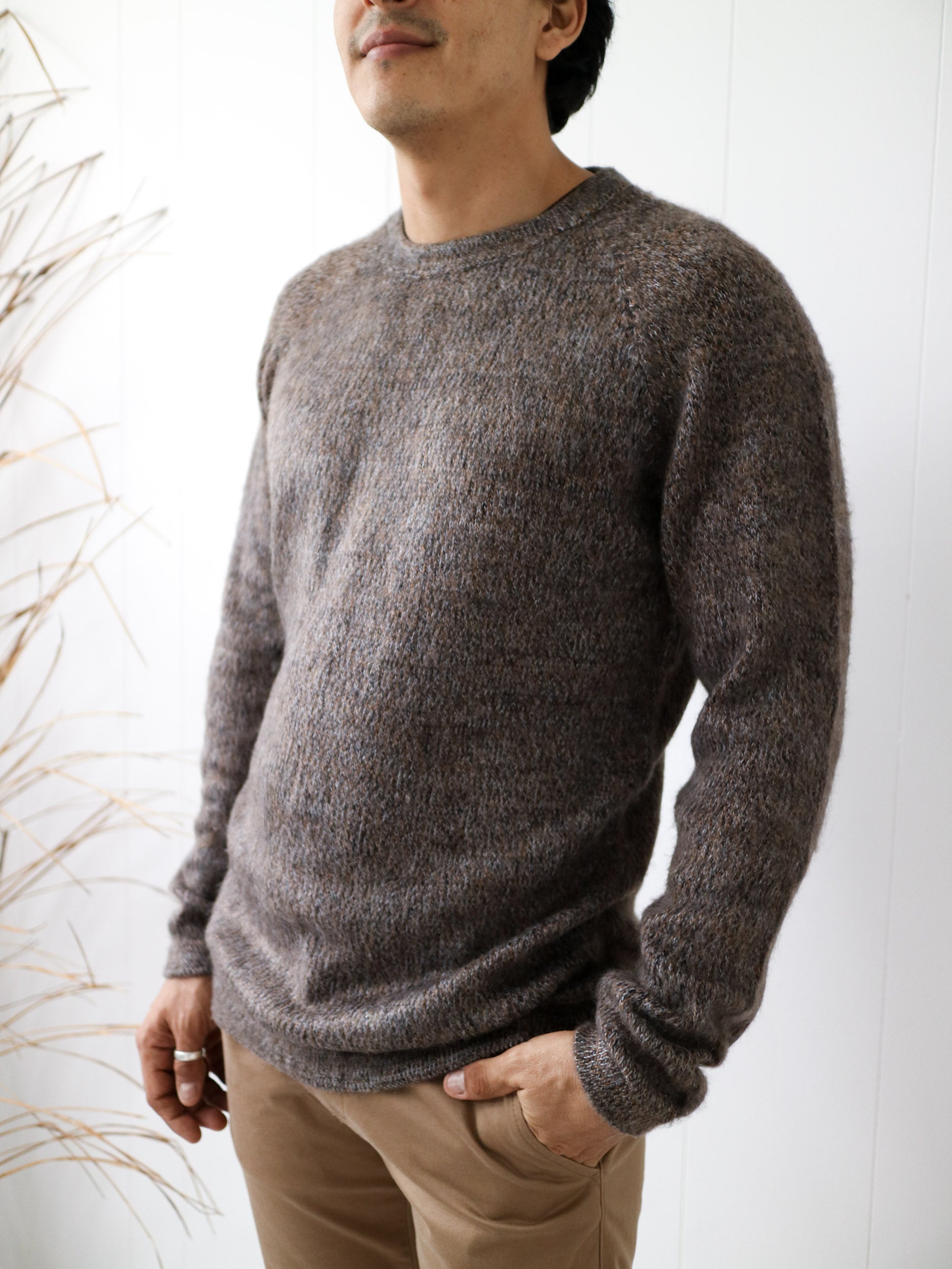 Man wearing a cozy, textured brown crewneck sweater and beige pants in a minimal setting