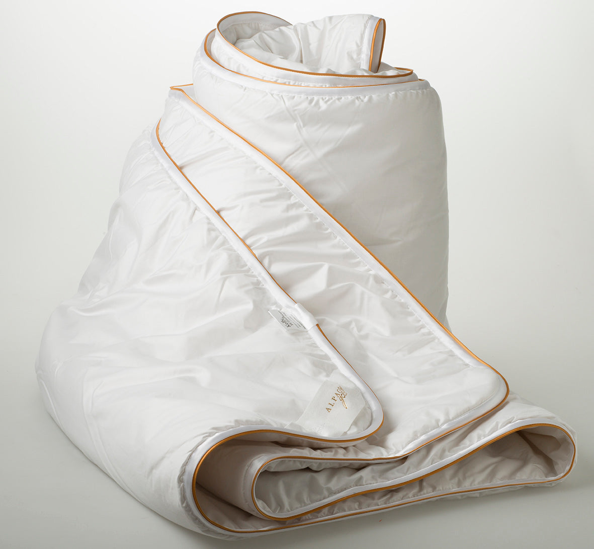Rolled white alpaca gold quilt with gold trim on a plain background