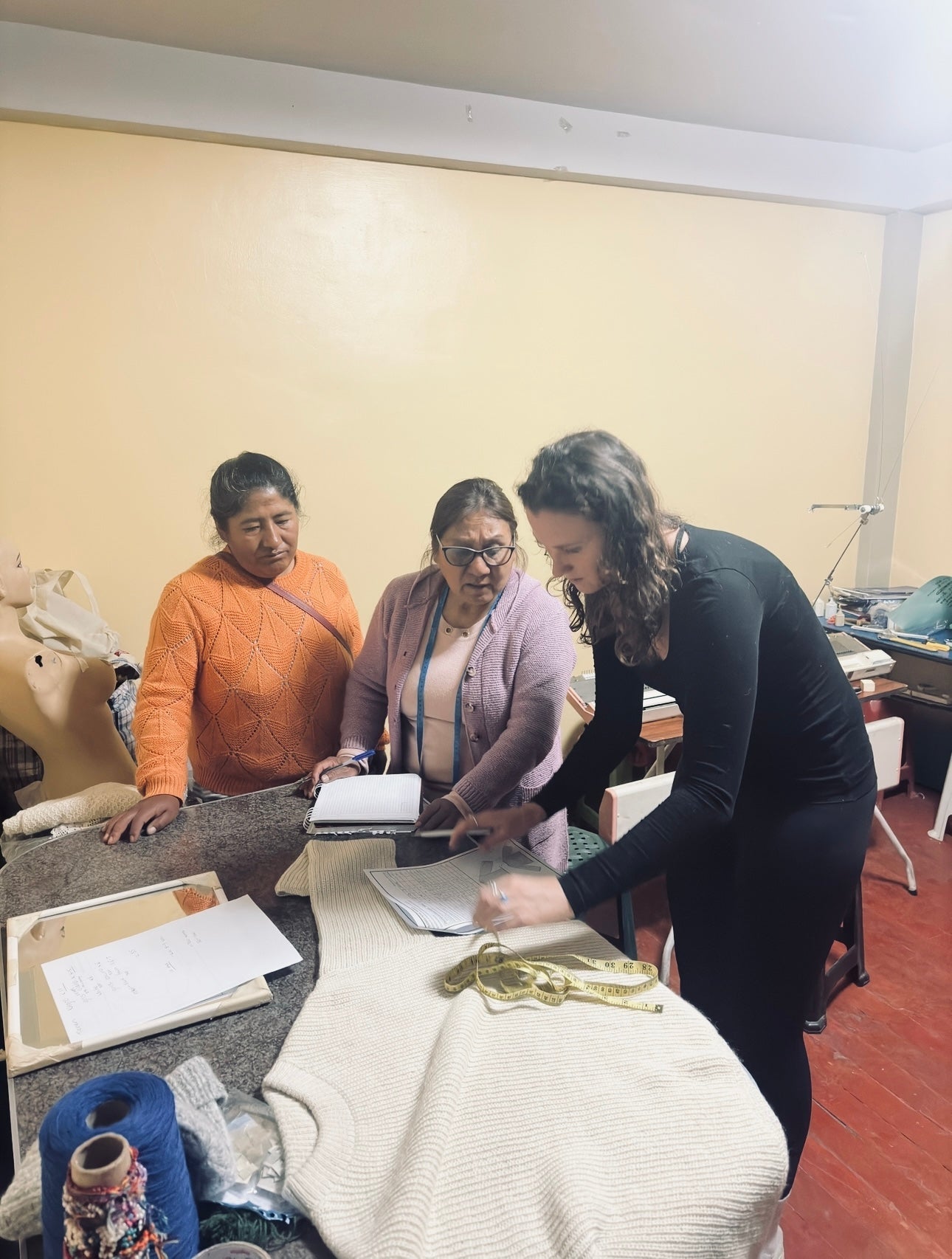 Three women collaborating over knitwear design samples and notes in a cozy workspace.