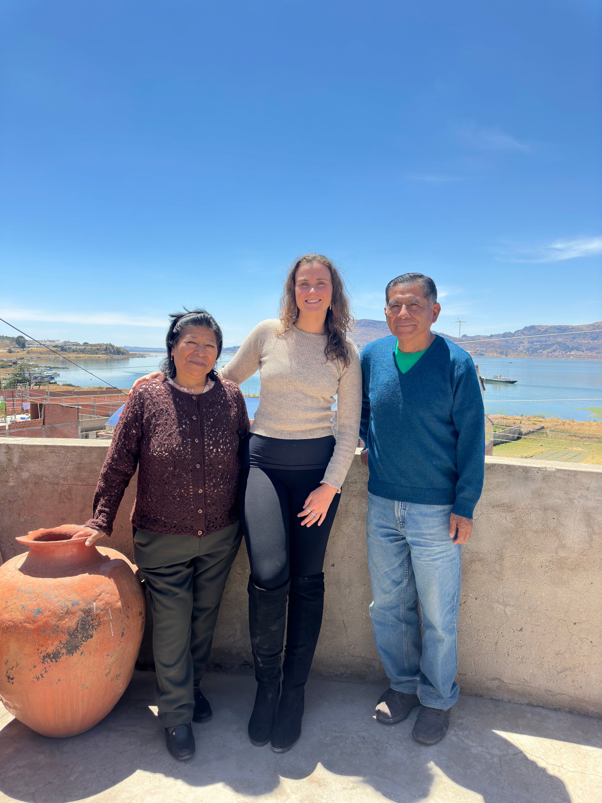 Three people standing on a terrace with a clay pot and scenic lake and mountain view in sunlight