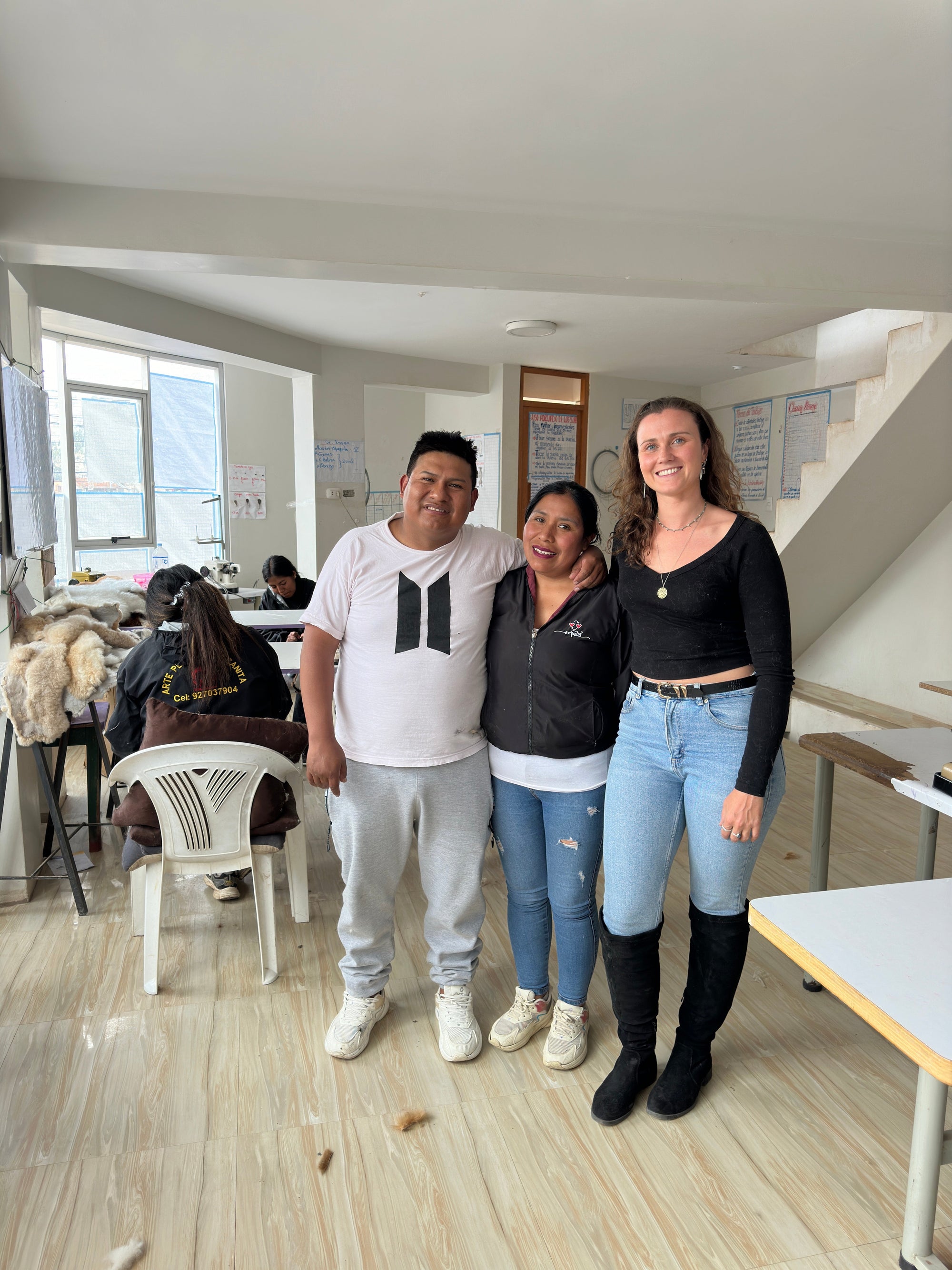 Three people smiling in a bright workshop with sewing tables and materials in the background