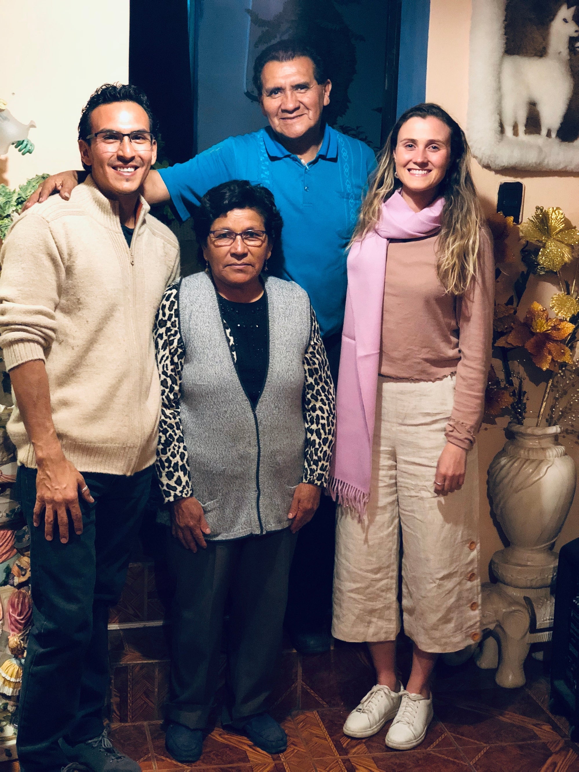 Group of four adults indoors, smiling, with alpaca wall art and floral decor in the background.