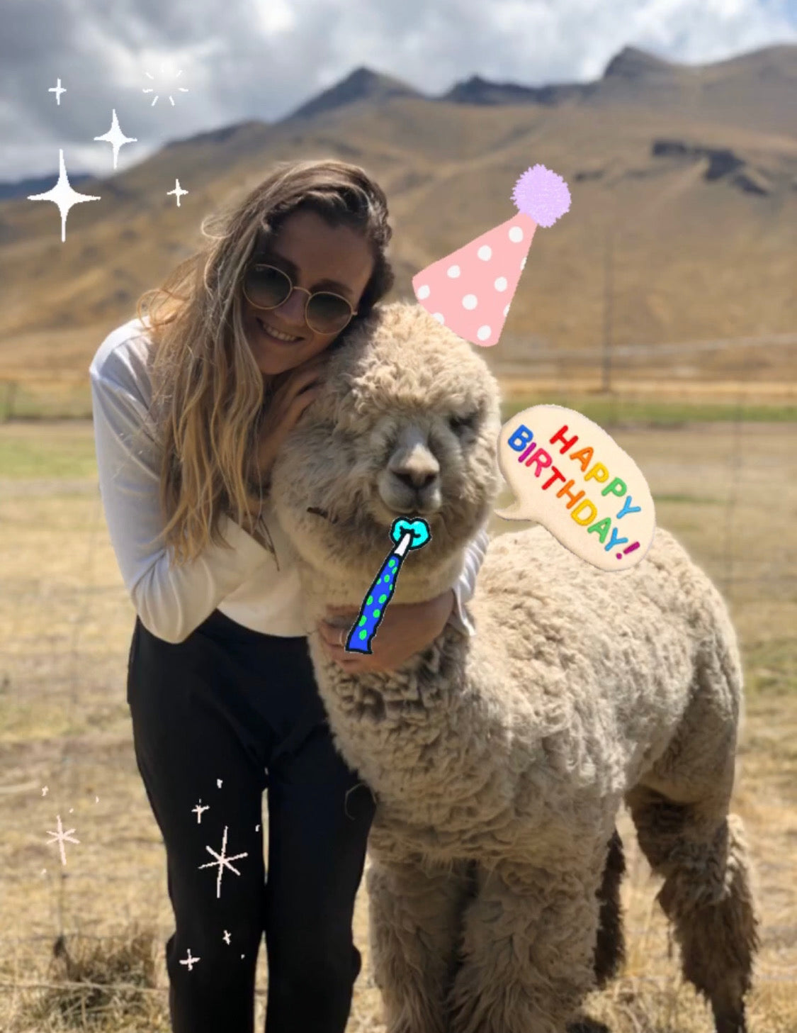 Woman hugging alpaca outdoors, decorated with birthday party hat and mountains in background