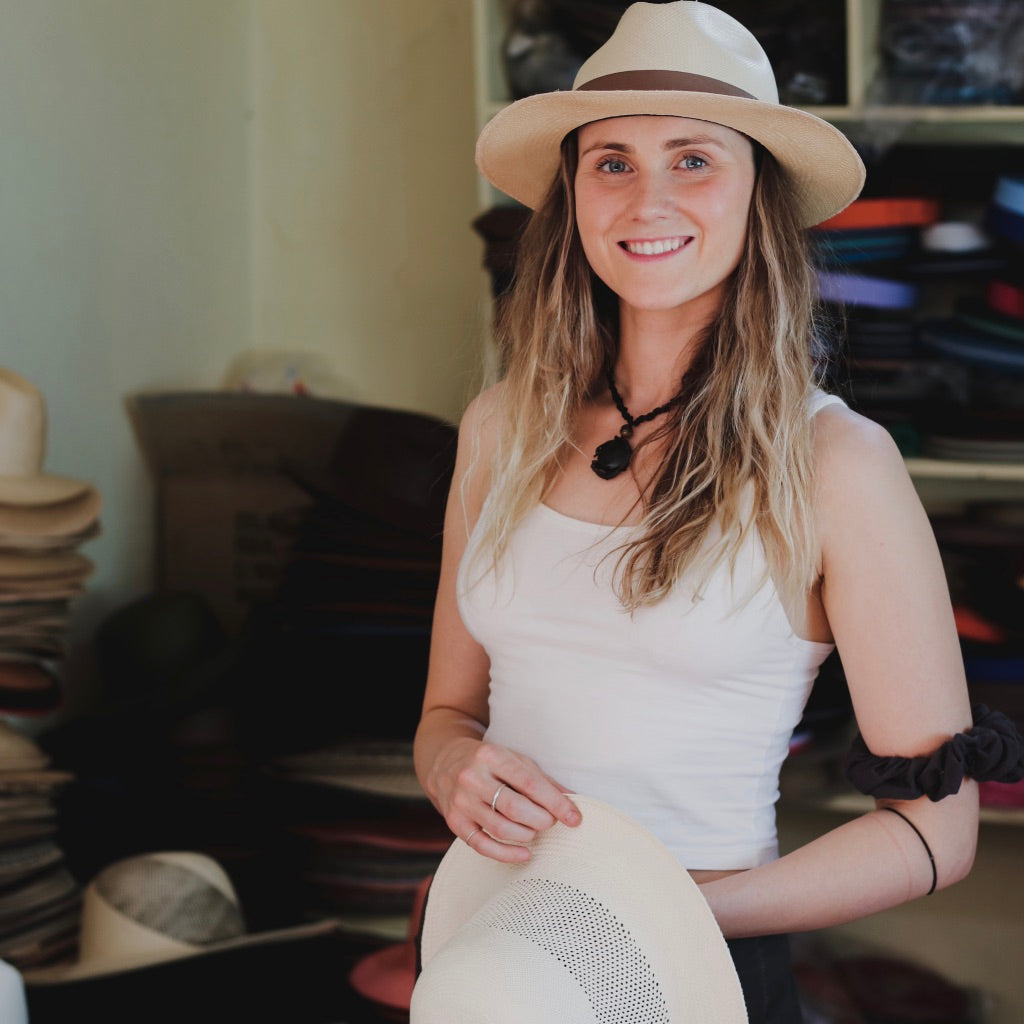 Woman wearing a Panama hat with a black ribbon band, and holding another hat with open weave crown