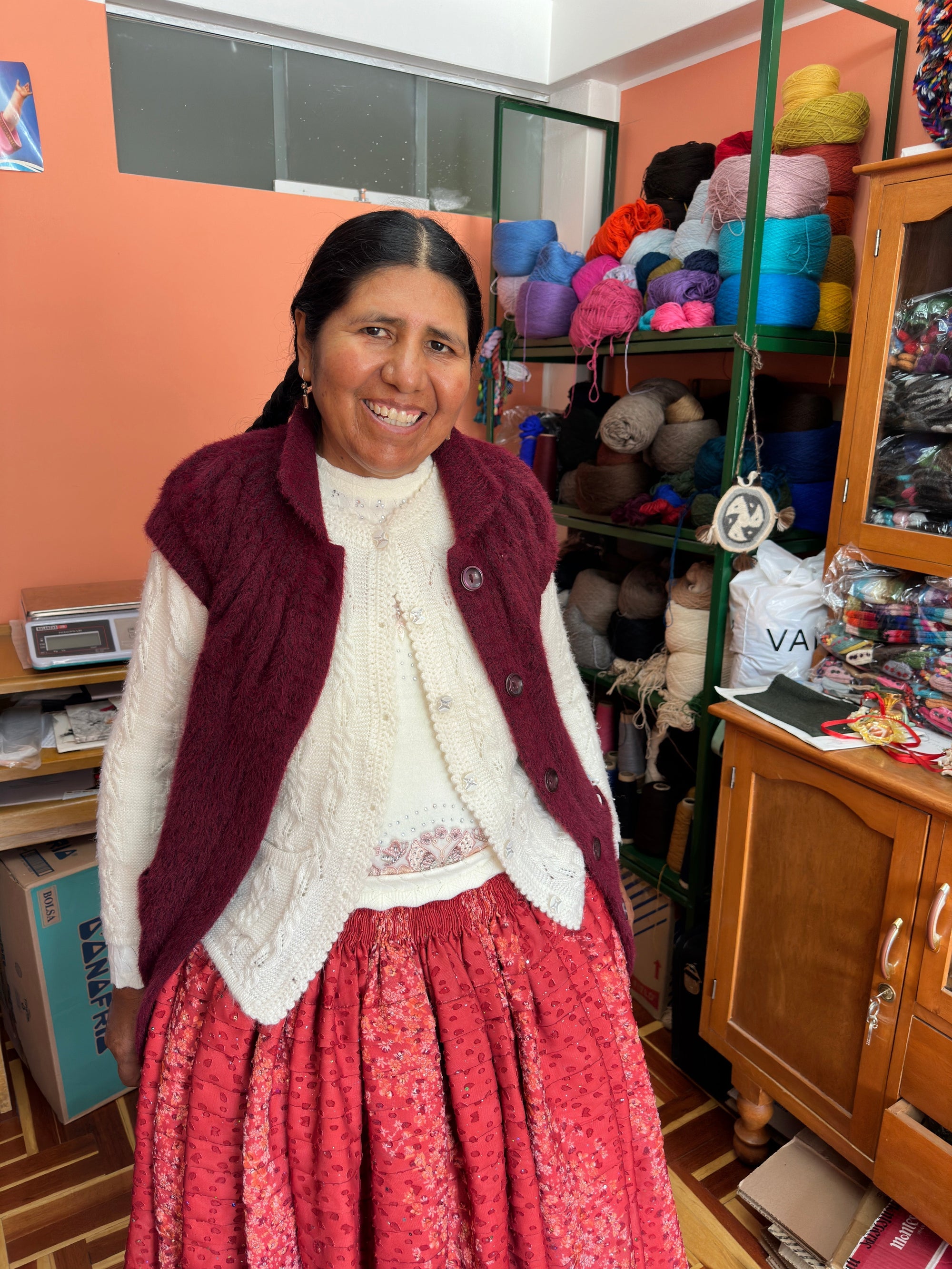 Woman in traditional clothing standing in yarn-filled workshop, artisan smiling