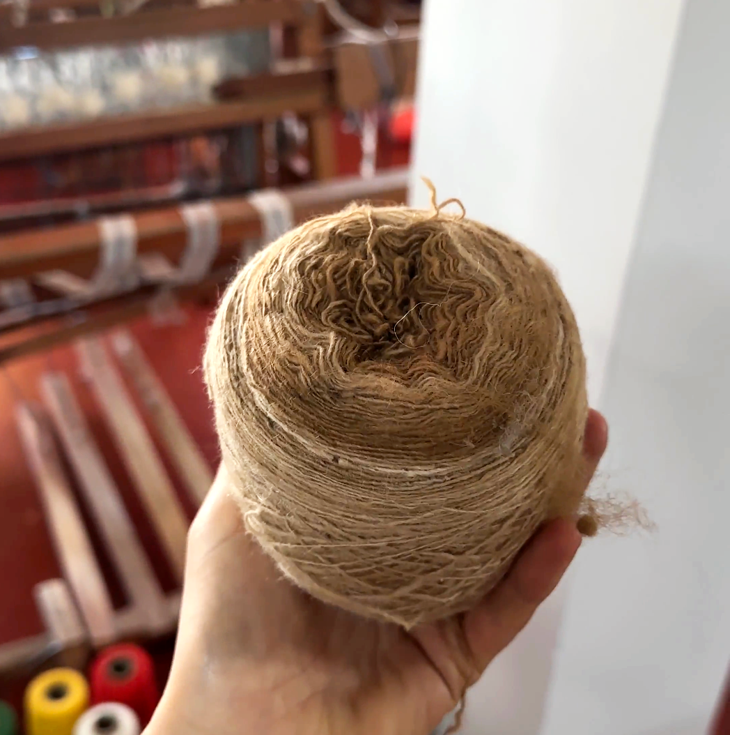 Hand holding a skein of natural brown alpaca yarn in a weaving workshop
