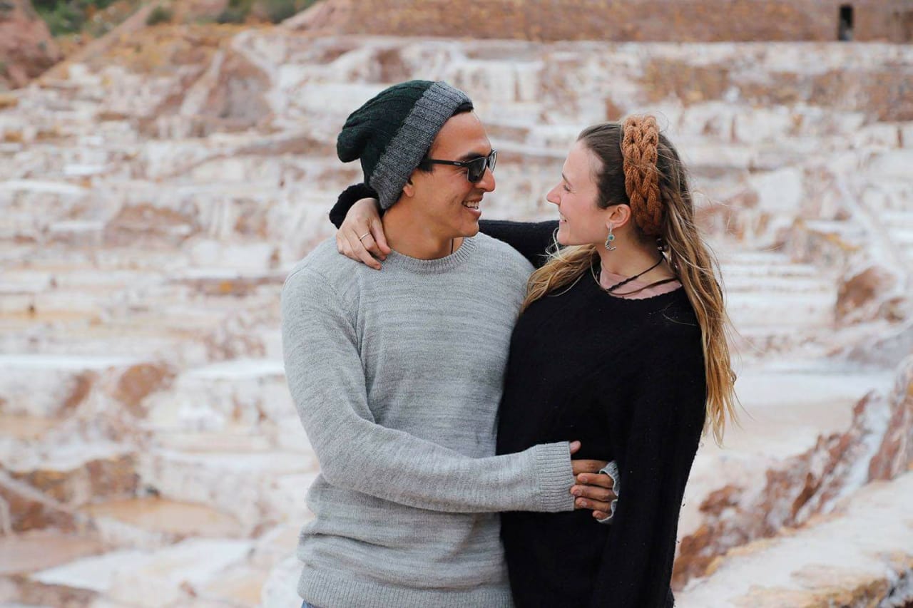 Smiling couple in cozy sweaters and hats embracing outdoors in a scenic rocky landscape