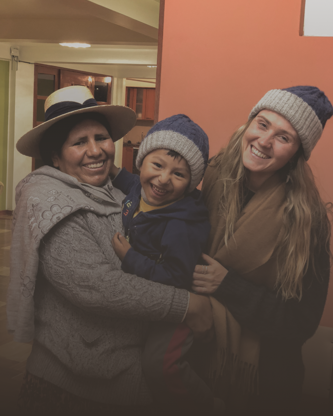Three people smiling, two women and a child, indoors, wearing winter clothing and hats.