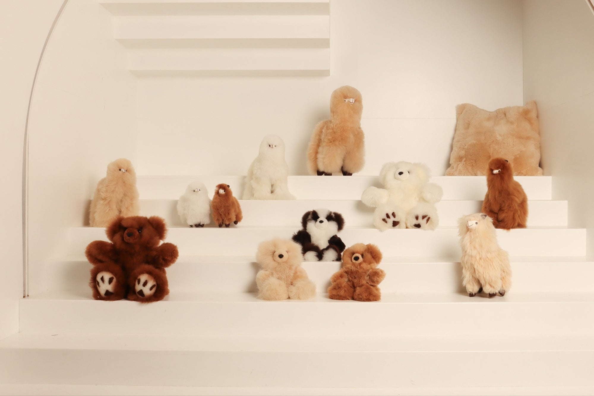 Assorted alpaca fleece plush toys and teddy bears arranged on white steps