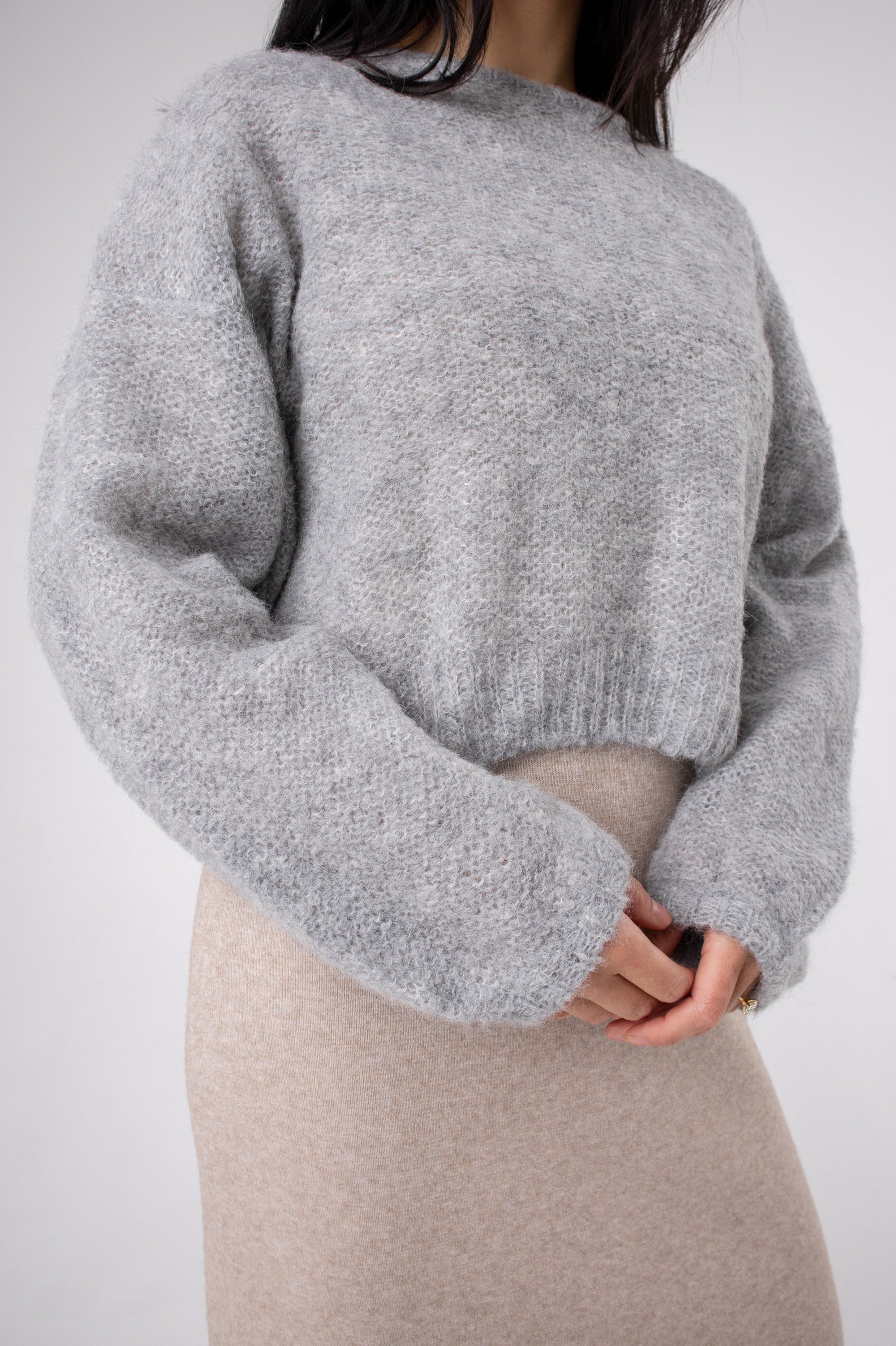 Soft grey alpaca jumper with long sleeves, worn by woman in neutral skirt