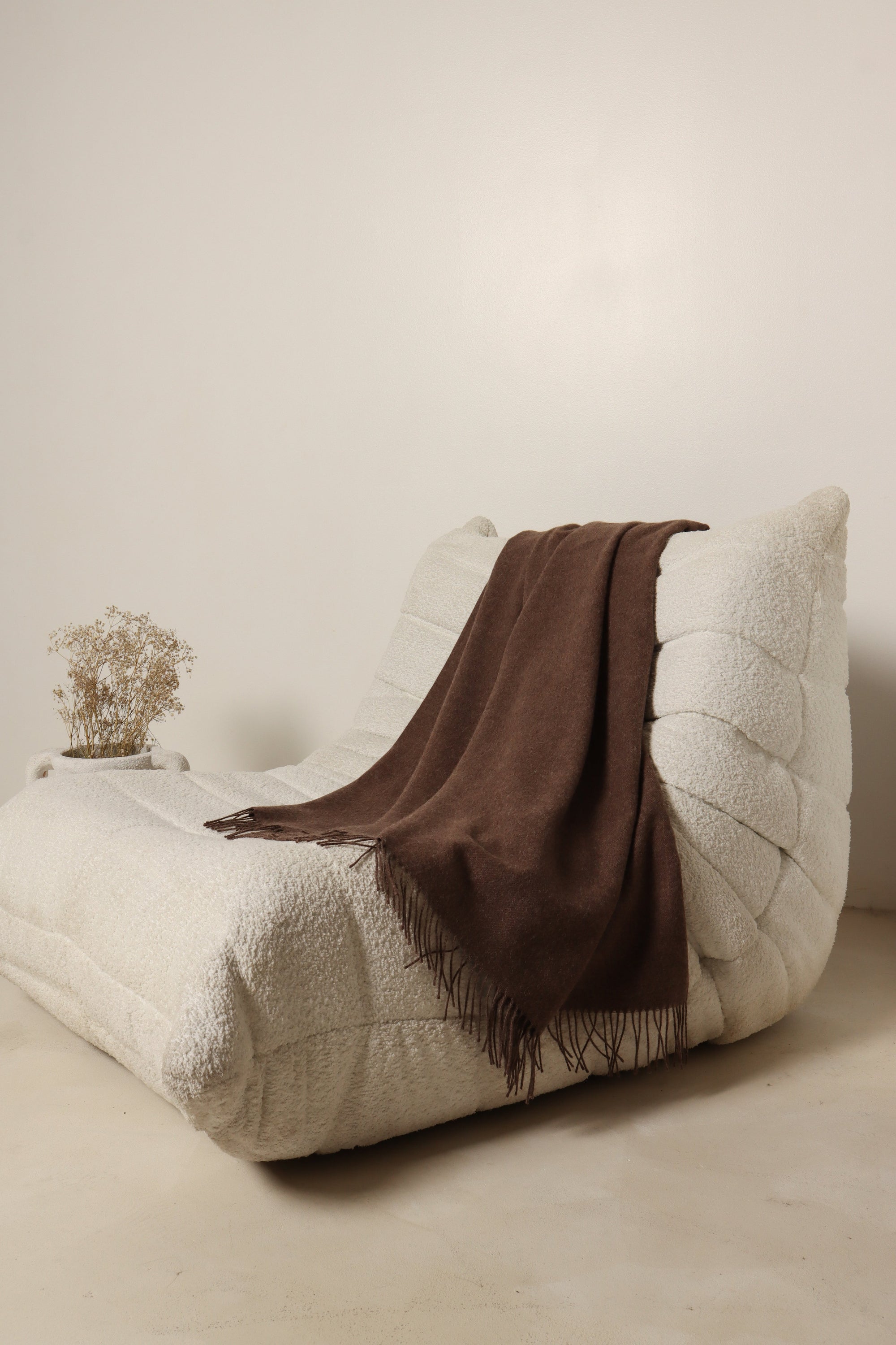 Modern cream lounge chair with brown throw blanket in minimalist living space