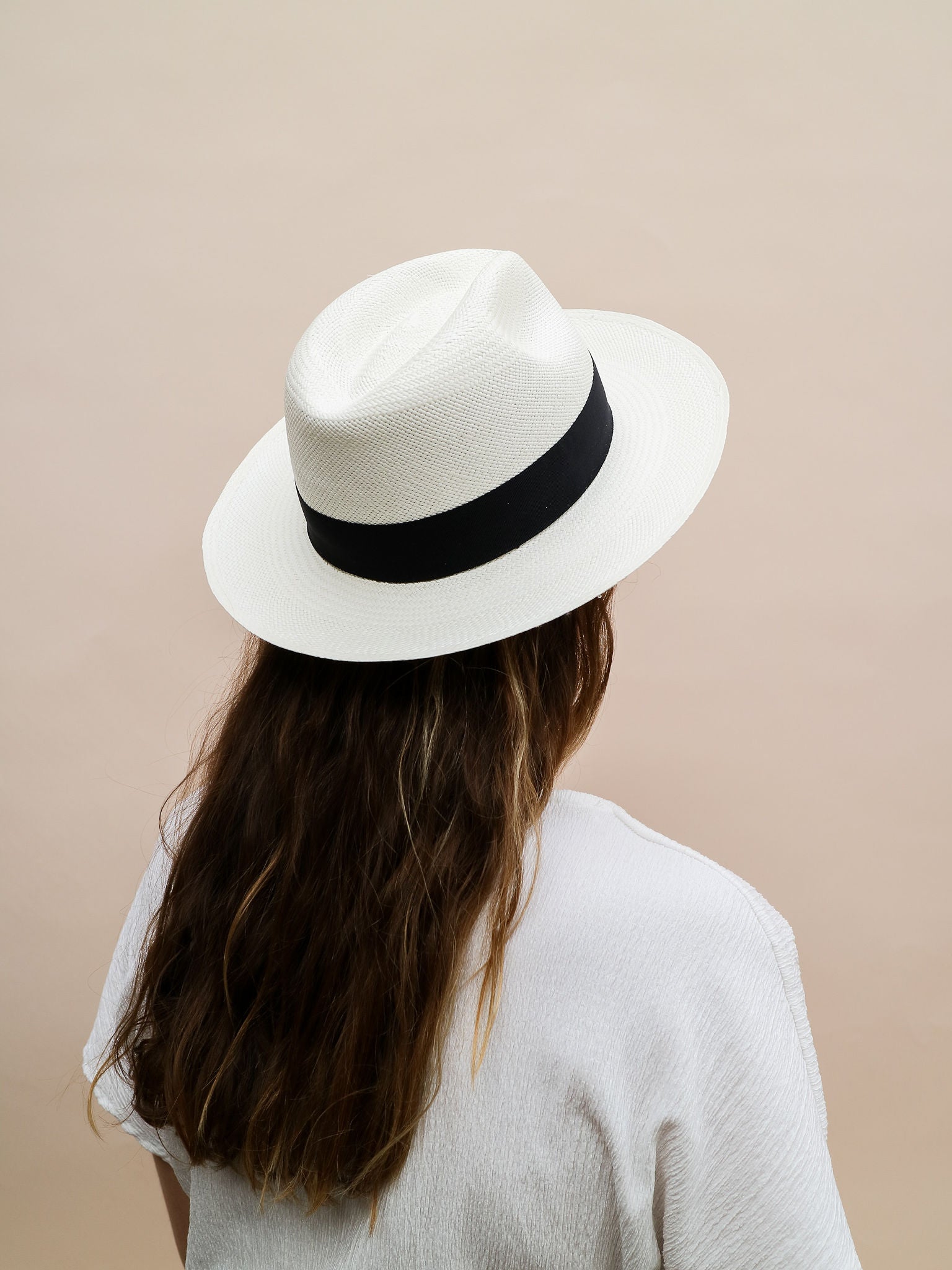 Woman in white textured shirt wearing white straw hat with black band, neutral background