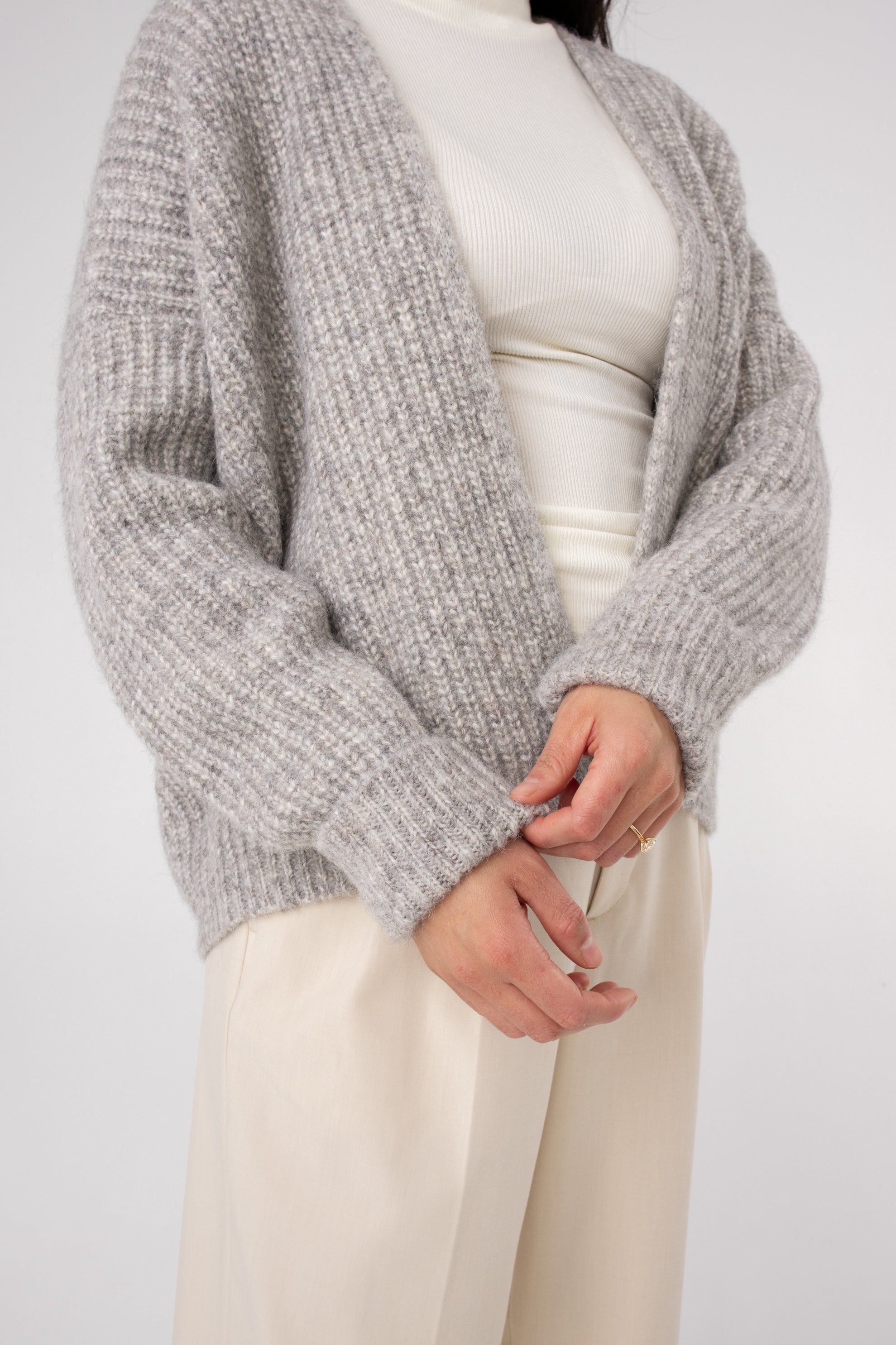Woman wearing a cozy textured grey knit cardigan over a white ribbed turtleneck